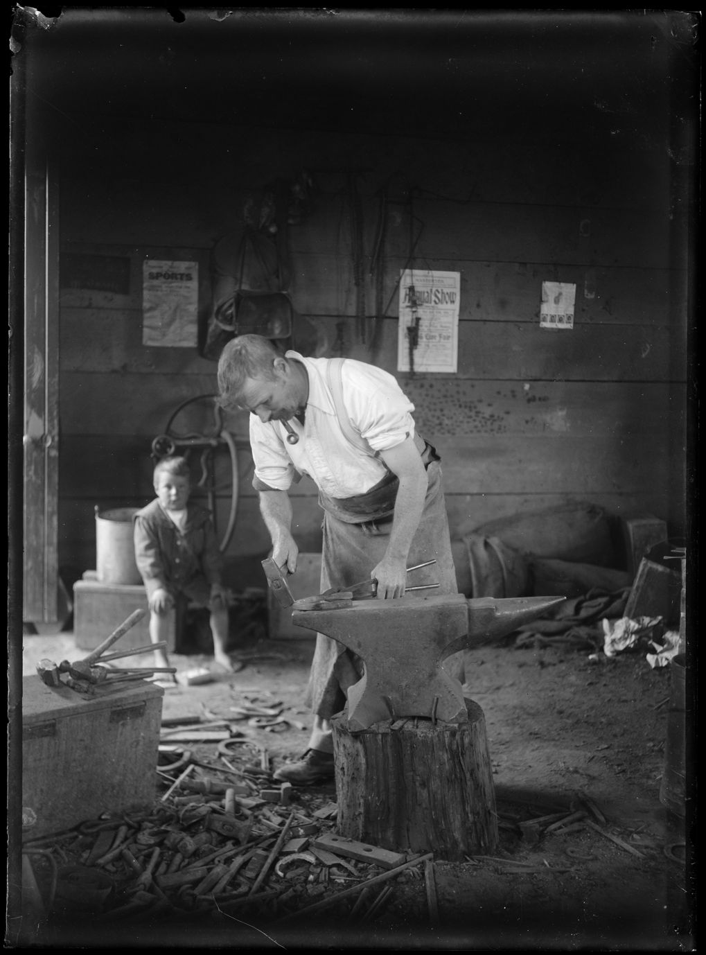 A New Zealand blacksmith working at an anvil in his forge around 1910